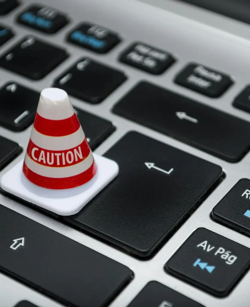 Cone de alerta com a palavra “Caution” sobre tecla Enter de um teclado, simbolizando cuidados com golpes online em 2025.